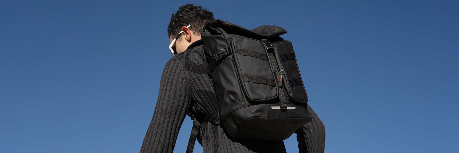 Man with Mark Ryden Global black backpack for spring travels under blue sky