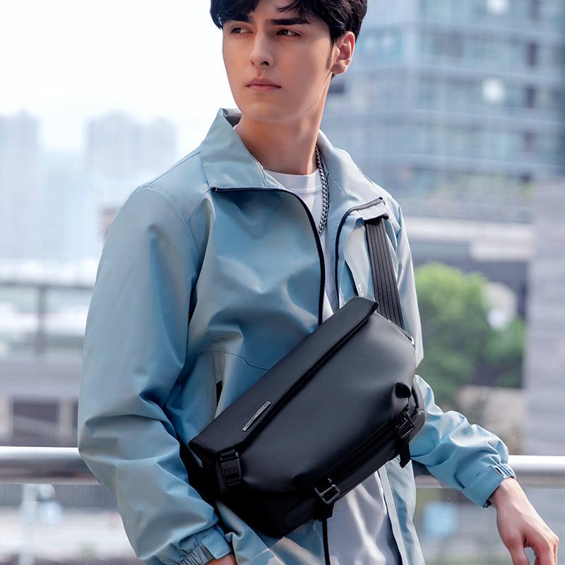Casual II black leather waterproof scratch-resistant stylish messenger bag worn by a person in a light blue jacket against an urban backdrop.
