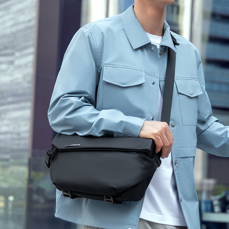 Black leather Casual II waterproof scratch-resistant messenger bag worn by a person in a light blue jacket and white shirt.