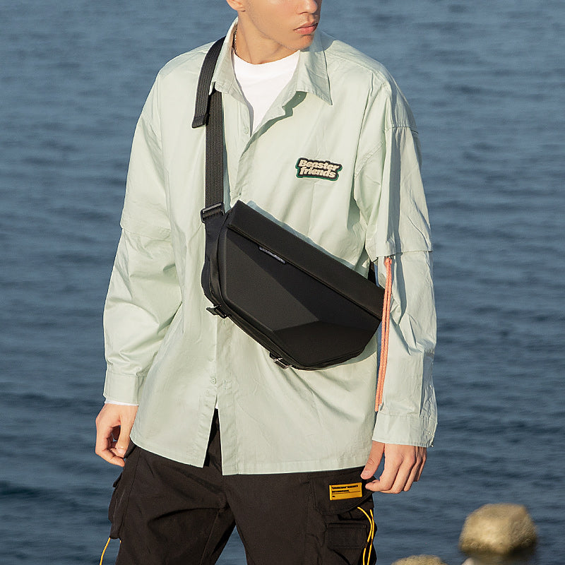 Black Diamond Facets large capacity waterproof scratch-resistant hard case crossbody bag worn over shoulder by model in light green shirt and black pants.