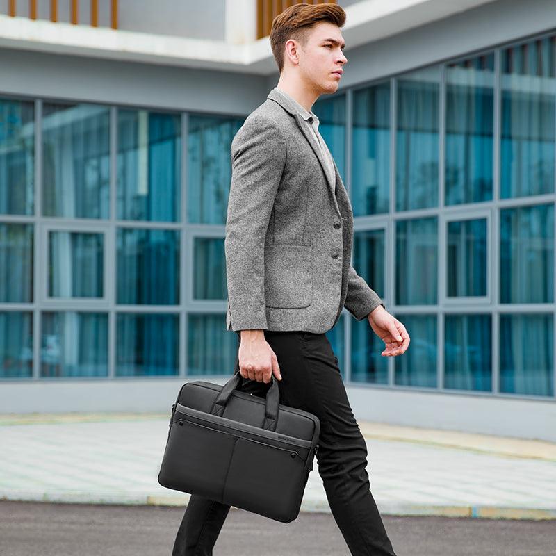 Man in gray blazer carries black MarkRyden tech commuter briefcase near modern glass building