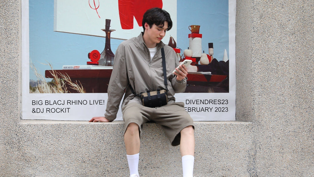 Traveler in gray outfit with Mark Ryden crossbody bag using phone near Lyon travel poster