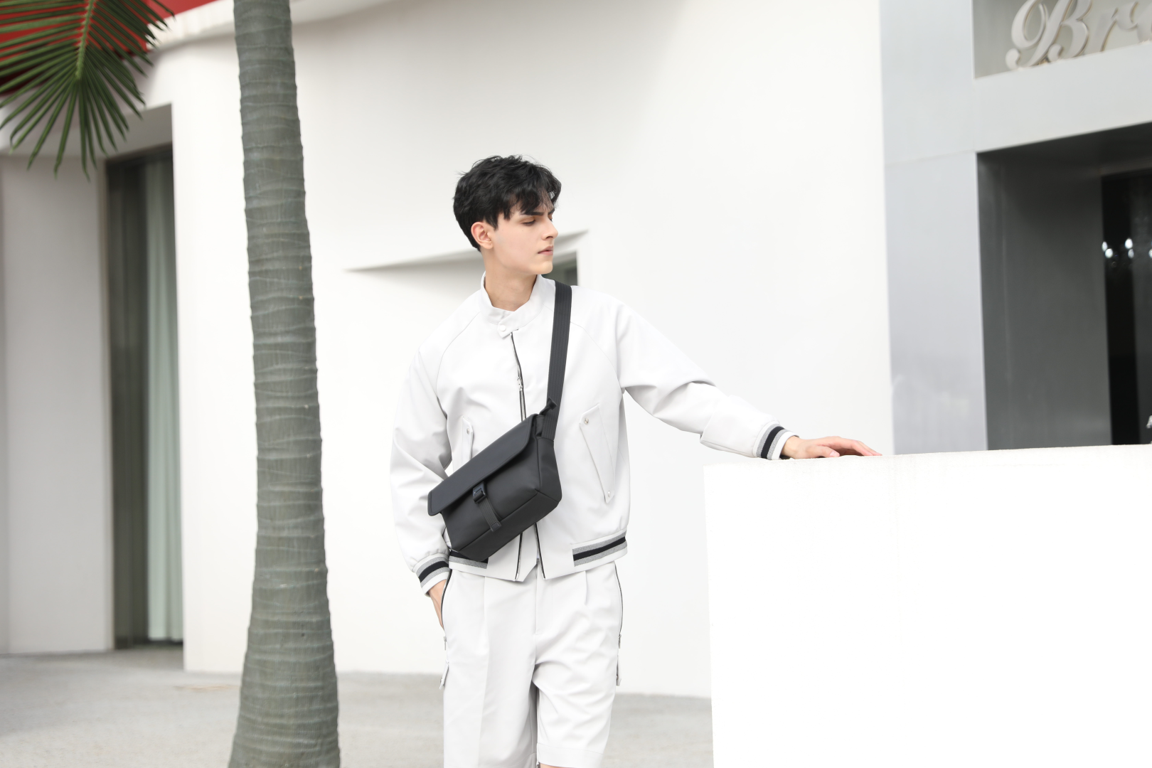 Mark Ryden Global men's anti-theft messenger bag in black, model in white sportswear, modern outdoor setting