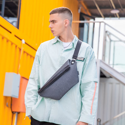 Gray chest bag with black strap on man in light green shirt at urban setting | MarkRyden Global