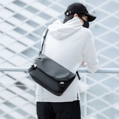 Mark Ryden Global: Black leather waterproof messenger bag on person in white hoodie