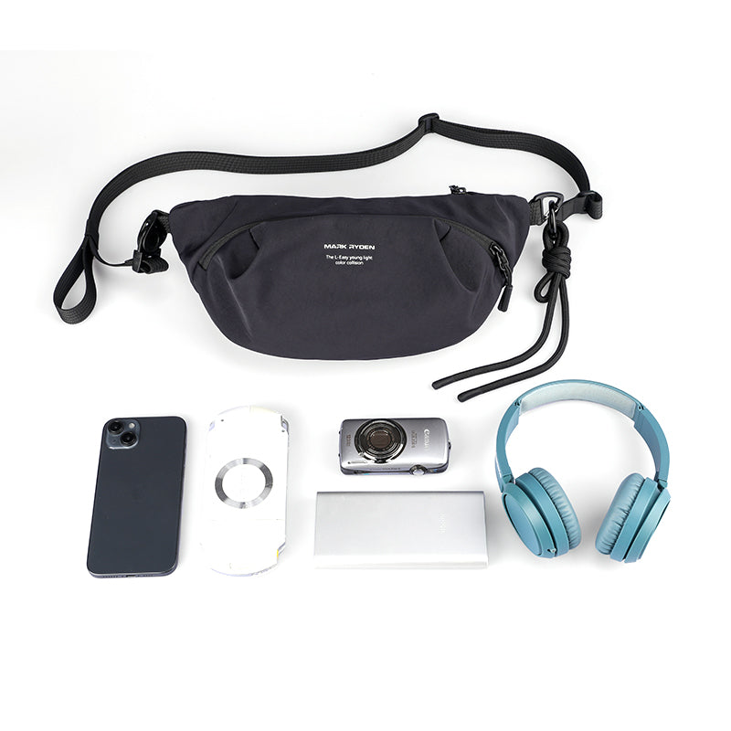 Black Mark Ryden ChillFlex sling bag with adjustable strap and zippered pocket, displayed with phone, camera, headphones, and other small essentials.
