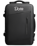 Black Mark Ryden backpack with personalized 'The Wedding Planner Dom' text, zippered front pocket, and durable design for modern travelers.