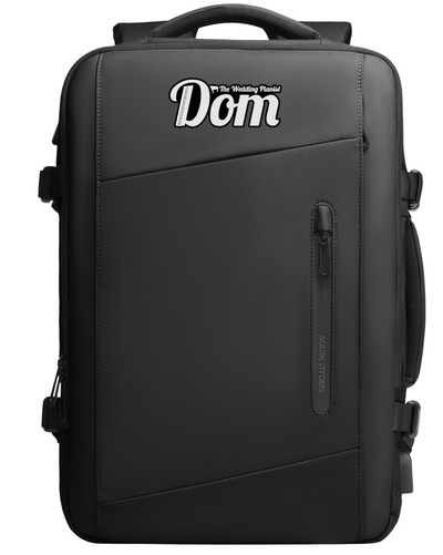 Black Mark Ryden backpack with personalized 'The Wedding Planner Dom' text, zippered front pocket, and durable design for modern travelers.
