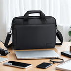 Black MarkRyden Tech Commuter Computer Briefcase 14/15.6 inch with dual handles and shoulder strap, displayed on a wooden desk with laptop, smartphones, and tech accessories.