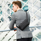 Man wearing black waterproof crossbody bag with multiple compartments over gray blazer, modern architectural backdrop | Mark Ryden Global