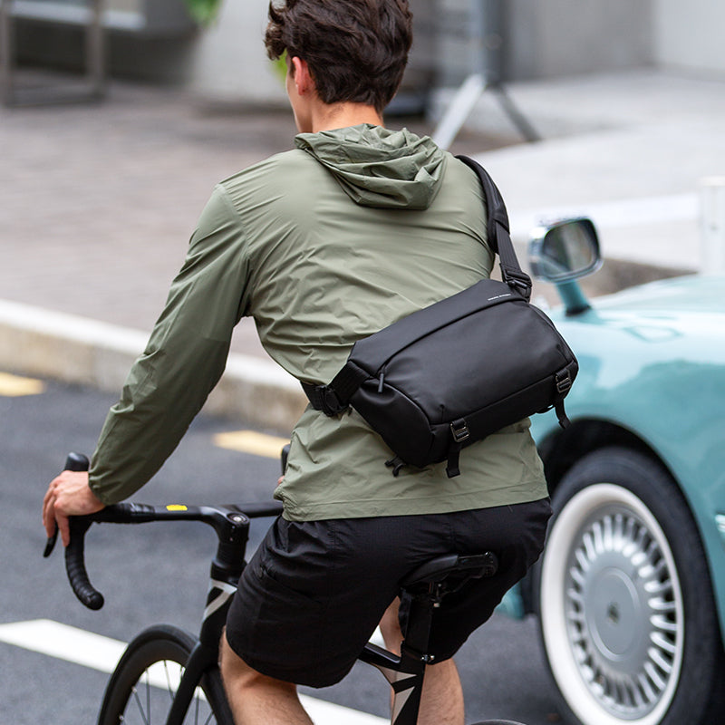 Man cycling with black spacious waterproof messenger bag by MarkRyden Global