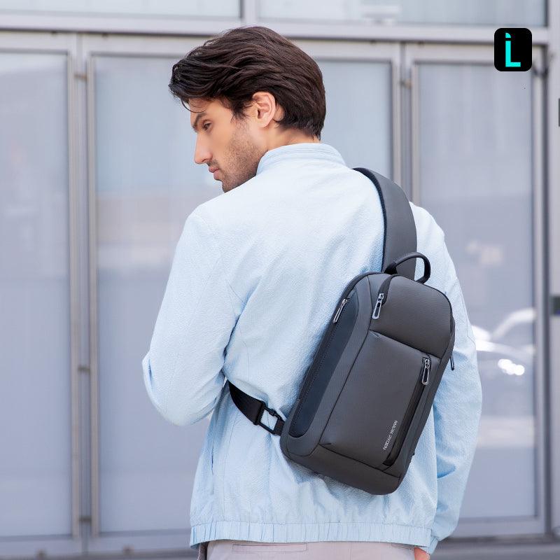 Mark Ryden Global's dark gray high-capacity crossbody bag with zippers, worn by man in light blue jacket outdoors.