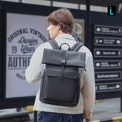 Man in beige coat wears Mark Ryden Global black minimalist backpack at city transit
