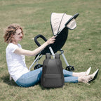 Dark gray Softologic I backpack, water-repellent and organized, placed on grass beside a stroller in a park with a woman sitting nearby.