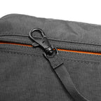 Close-up of dark gray AeroSling ultra-light anti-theft crossbody bag with black carabiner attached to orange-accented zipper, textured fabric, and RFID-Safe technology.
