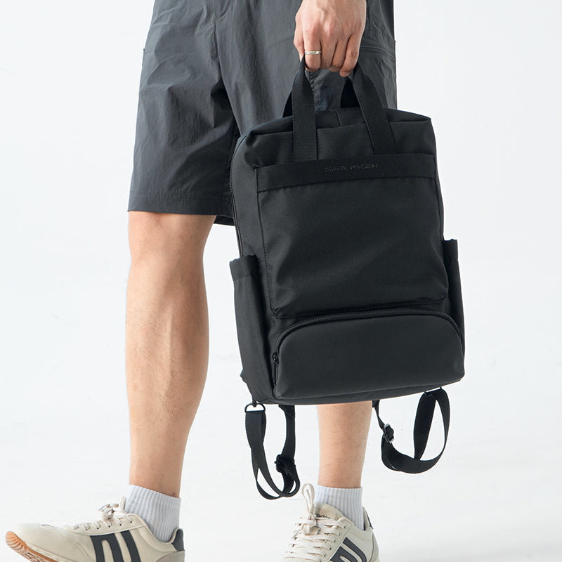 Black Mark Ryden BreezePack lightweight backpack with removable shoulder straps and front zippered pocket, held by a person in gray shorts and white sneakers.