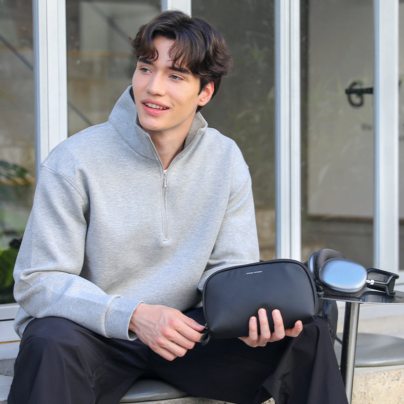 Man in gray quarter-zip pullover holds black NanoGrid digital toolkit bag near headphones | MarkRyden Global