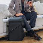 Black AeroShield 2025 innovative durable waterproof anti-theft backpack with smooth material and sleek design, positioned next to a person on a light gray couch in a modern indoor setting.