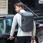 Dark gray AeroShield 2025 durable waterproof backpack with sleek angular design, worn by man near black car in urban setting.