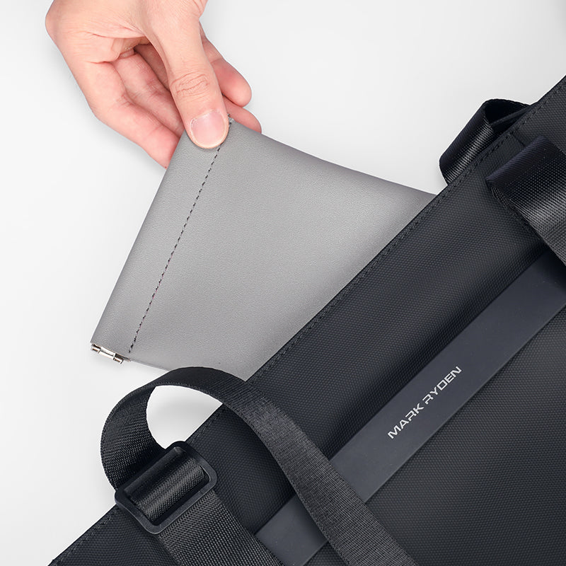 Gray Mark Ryden coin pouch with secure zipper closure being held next to black backpack, designed for effortless carry of valuables.