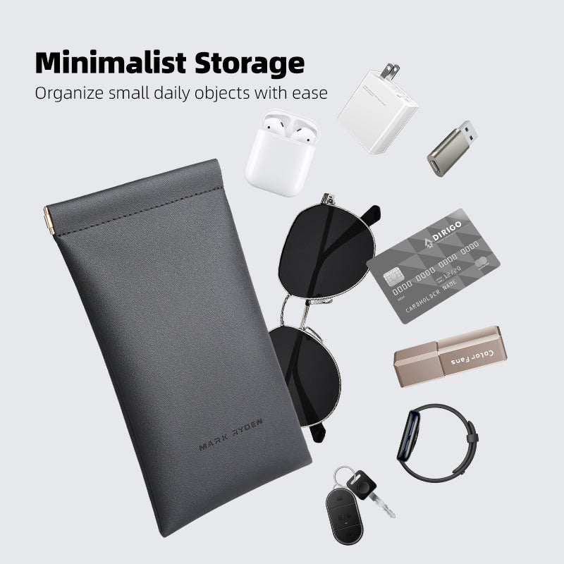 Gray Mark Ryden minimalist storage pouch with sleek design, perfect for carrying sunglasses, eyeglasses, or data cables, surrounded by small daily items like AirPods, charger, USB drive, card, smartwatch, and keys.