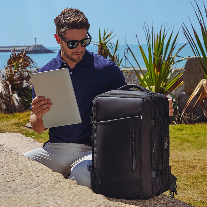 Mark Ryden black anti-theft compression backpack with man using tablet by ocean